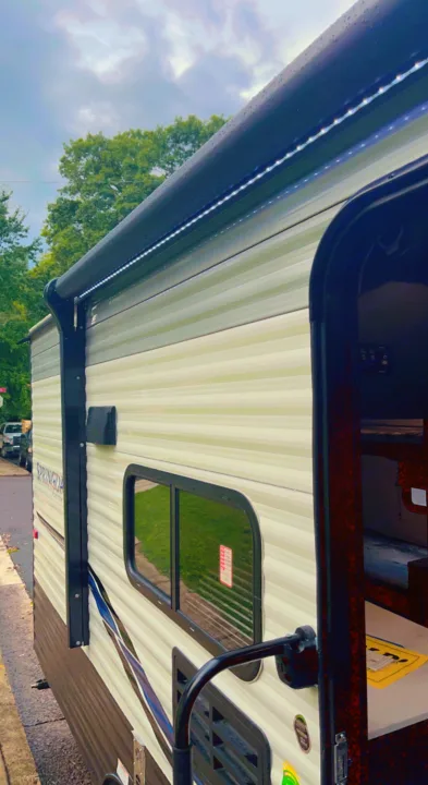 Side profile of a clean **RV rental** with illuminated awning and open door. Window reflects lush trees and clouds.. Keystone RV Springdale 2022