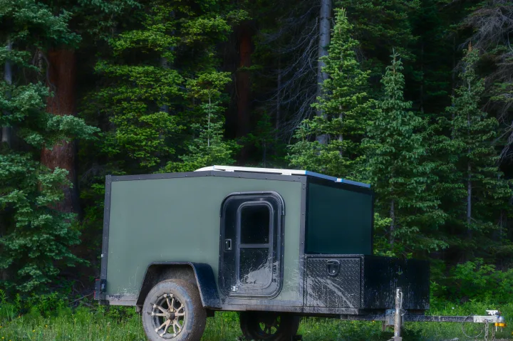 Mud-splattered green off-road RV rental trailer nestled in a dense forest, ready for adventure.. White River X Camper Trail Explorer 2021