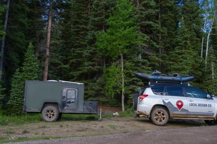 Adventure-ready: an RV rental trailer and SUV with raft, parked by a dense forest. Ideal for exploring nature.. White River X Camper Trail Explorer 2021