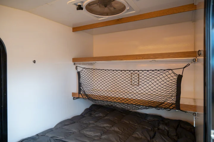 Cozy RV rental interior with a bed, overhead shelf, and practical cargo net storage.. White River X Camper Trail Explorer 2021