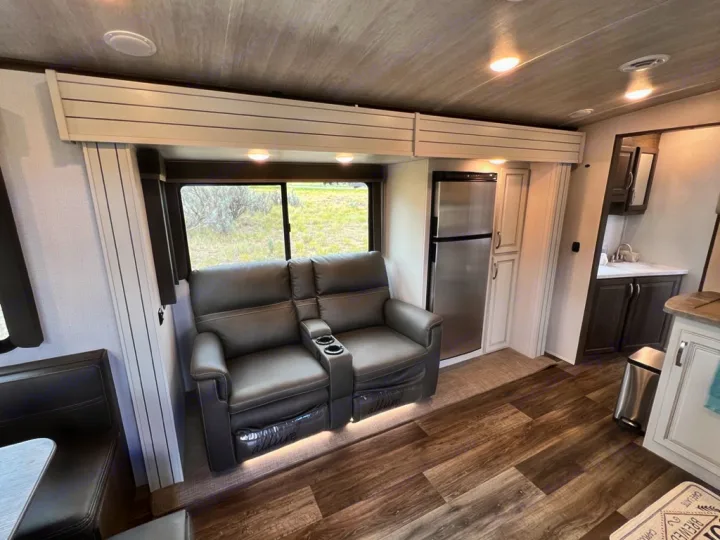 Comfortable RV rental interior featuring recliners, a scenic window view, refrigerator, and dining nook.. Keystone RV Cougar 2022