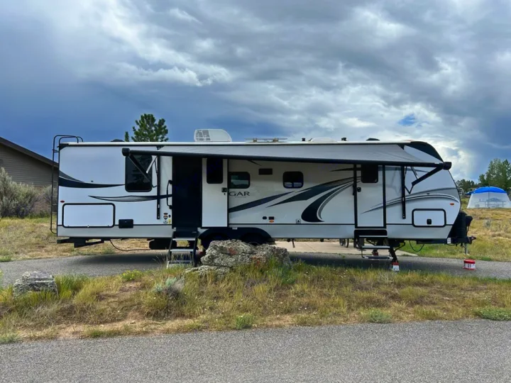 This rv rental, a white travel trailer, is set up at a scenic campground under cloudy skies, ready for outdoor adventure.. Keystone RV Cougar 2022