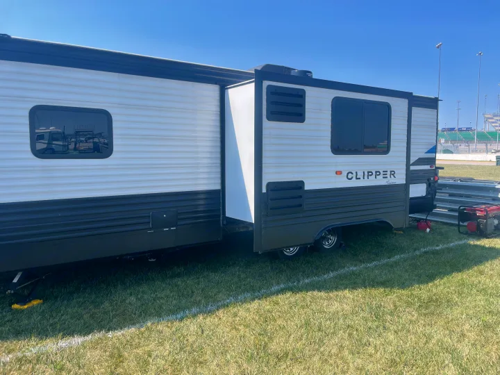 Clipper RV rental with slide-out extended, parked on grass at an outdoor event. Generator visible. Perfect for trackside stays.. Coachmen Clipper 26BHS 2021