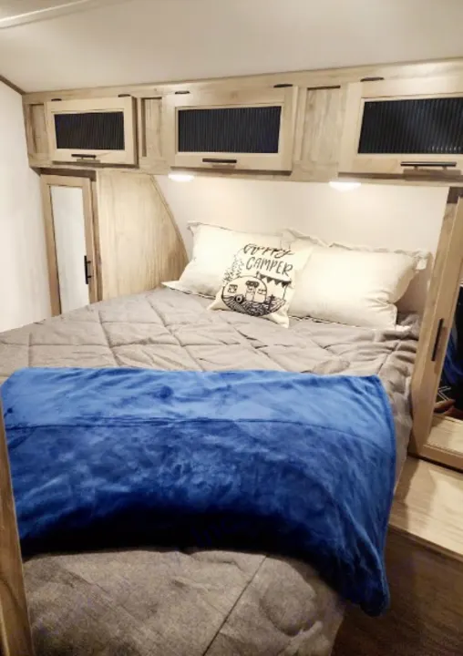 Cozy RV rental bedroom featuring a comfy bed, "Happy Camper" pillow, and overhead storage cabinets.. Forest River Cherokee Alpha Wolf 2022