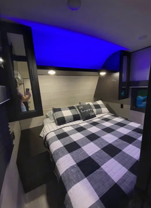 Cozy RV rental bedroom with buffalo plaid bedding, blue ambient lights, and mirrored storage.. Jayco 267 BHS 2022