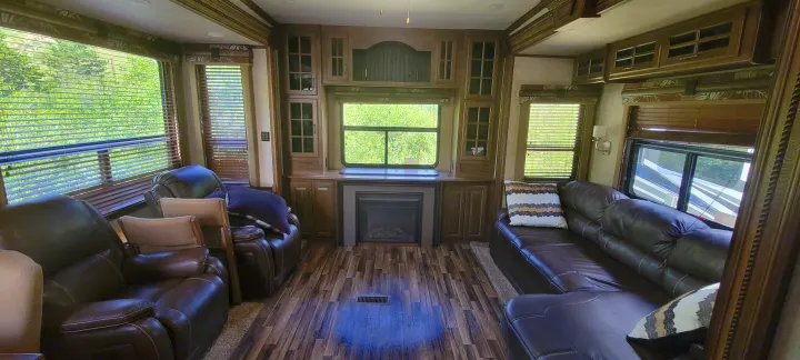 Spacious RV rental living area with brown leather recliners, a sectional sofa, fireplace, and windows with blinds.. Keystone RV Alpine 2015