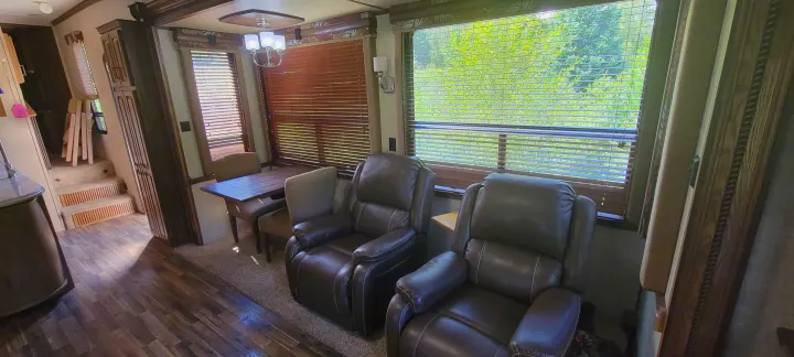 Relaxing RV rental interior with recliners, dining table, and stairs, offering a view of nature.. Keystone RV Alpine 2015
