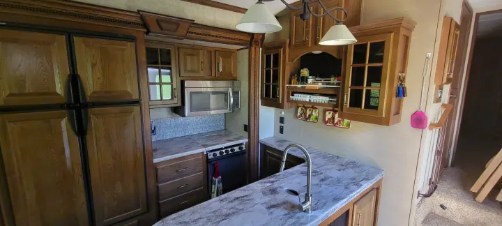 Well-equipped RV rental kitchen featuring a full-size fridge, microwave, stove, sink, and ample wooden cabinets with light countertops.. Keystone RV Alpine 2015
