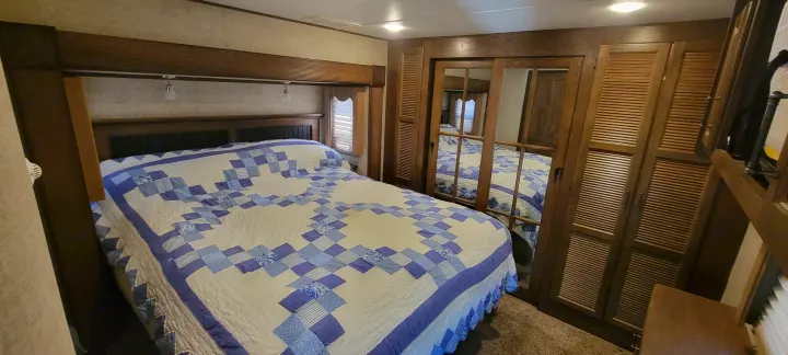 Cozy RV rental bedroom with a blue patterned quilt, wood headboard, and mirrored closet doors reflecting the bed.. Keystone RV Alpine 2015