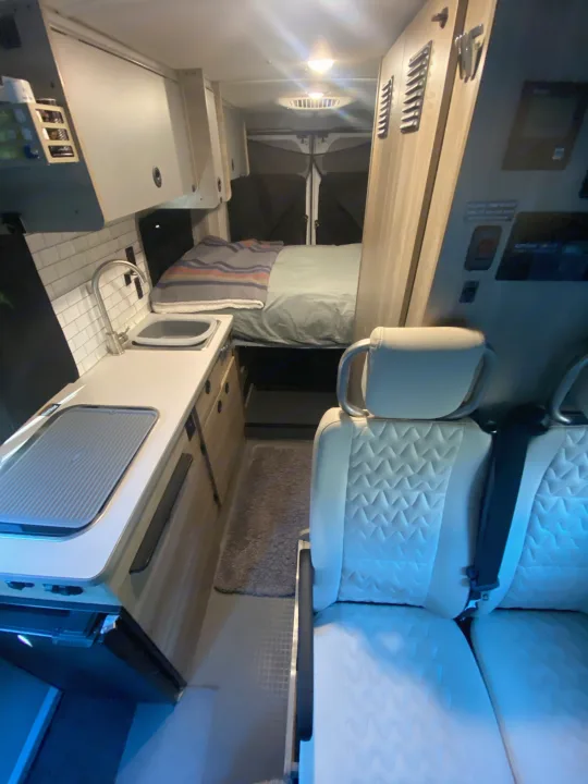 View inside a modern rv rental camper van, revealing a compact kitchen, comfortable bed, and quilted seating area.. Winnebago Solis P 2021