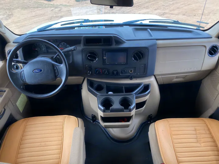 Inside an RV rental: Dashboard and front cabin of a Ford E-Series van with steering wheel, controls, and seating.. Winnebago Minnie Winnie 2015