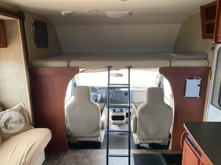 Inside this RV rental: a cozy over-cab bunk bed with ladder, overlooking the driver's cabin and dashboard.. Winnebago Minnie Winnie 2015