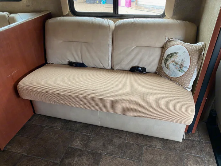 Cozy RV dinette bench with a ribbed beige slipcover, seatbelts, and a fish pillow. Ideal for an rv rental.. Winnebago Minnie Winnie 2015