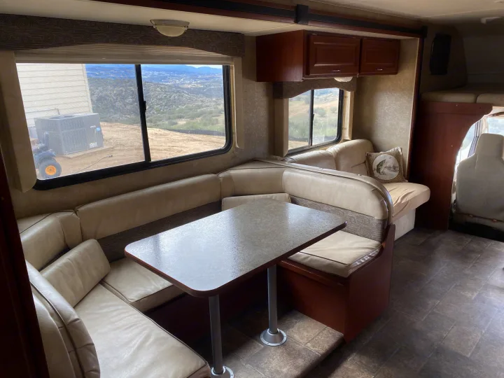 RV rental interior: U-shaped dining booth with table, sofa, and wide windows revealing a mountainous landscape.. Winnebago Minnie Winnie 2015