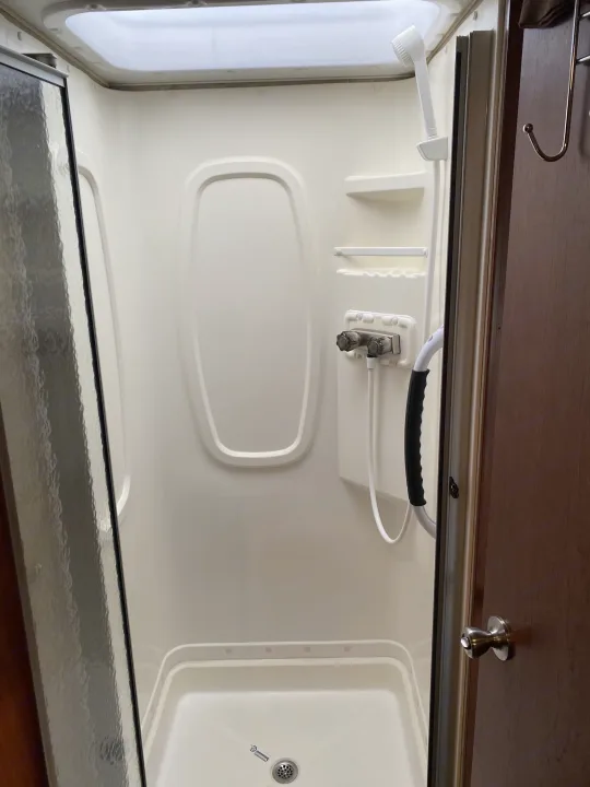 Inside this RV rental, a clean, compact shower stall with a skylight, handheld shower, and water controls.. Winnebago Minnie Winnie 2015