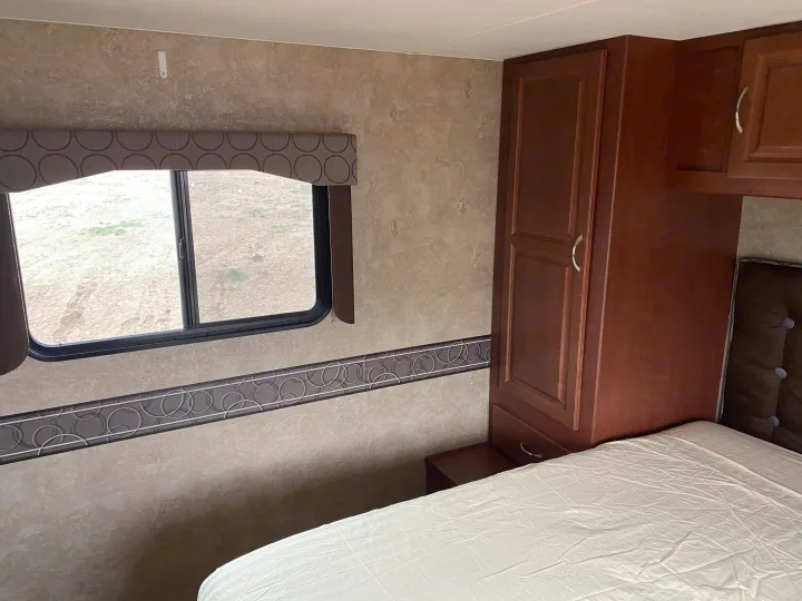 Inside an RV rental: a cozy bedroom with a bed, large window, and dark wood cabinetry. Wall hooks add convenience.. Winnebago Minnie Winnie 2015