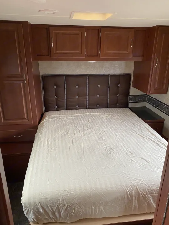 Cozy RV rental bedroom features a comfy bed, padded headboard, and ample storage cabinets for your travels.. Winnebago Minnie Winnie 2015