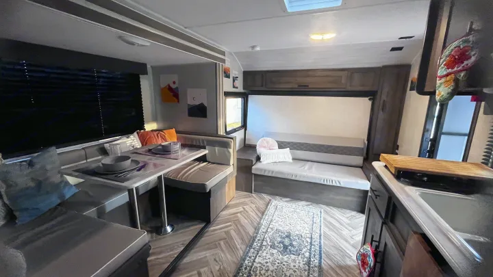 Cozy RV rental interior with a U-shaped dining booth, long sofa, patterned rug, and a compact kitchen. Ideal travel space.. Forest River Wildwood FSX 2021