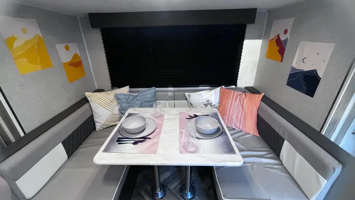 Modern RV rental dining area featuring a white table, grey benches with colorful pillows, and mountain art on the walls.. Forest River Wildwood FSX 2021