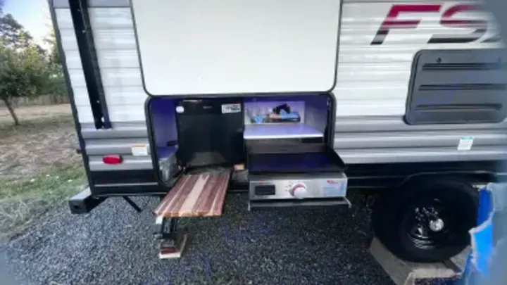 This RV rental's outdoor kitchen boasts a griddle, fridge & prep area. Ideal for camping meals.. Forest River Wildwood FSX 2021