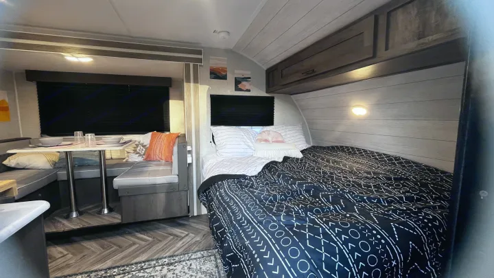 Cozy RV rental interior. Features a comfy bed with a black and white patterned comforter and a bright dinette area.. Forest River Wildwood FSX 2021