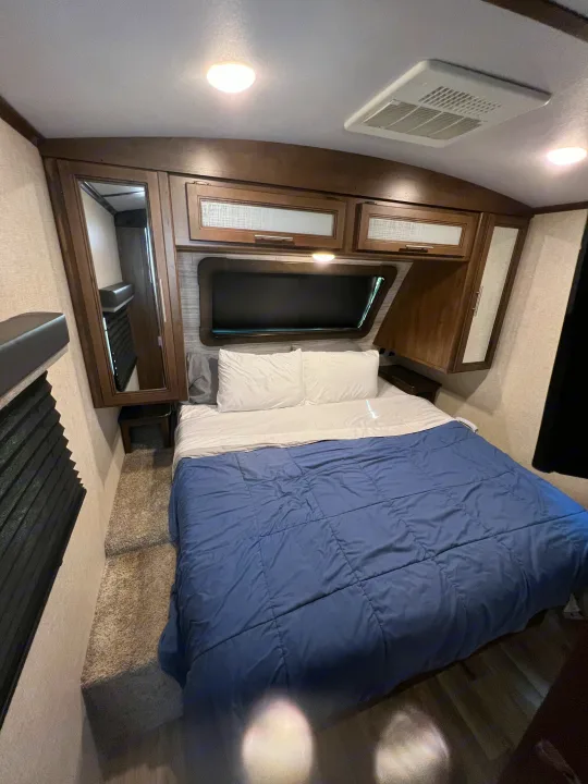 Experience comfort in this RV rental bedroom. Features include a bed, overhead cabinets, air conditioning, and a mirror.. Keystone Cougar Half-Ton 2021