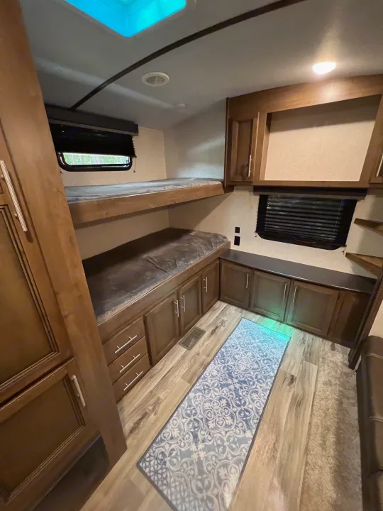 Spacious RV rental bunkhouse featuring two beds, wooden cabinets with storage, wood-look flooring, and a blue patterned rug.. Keystone Cougar Half-Ton 2021