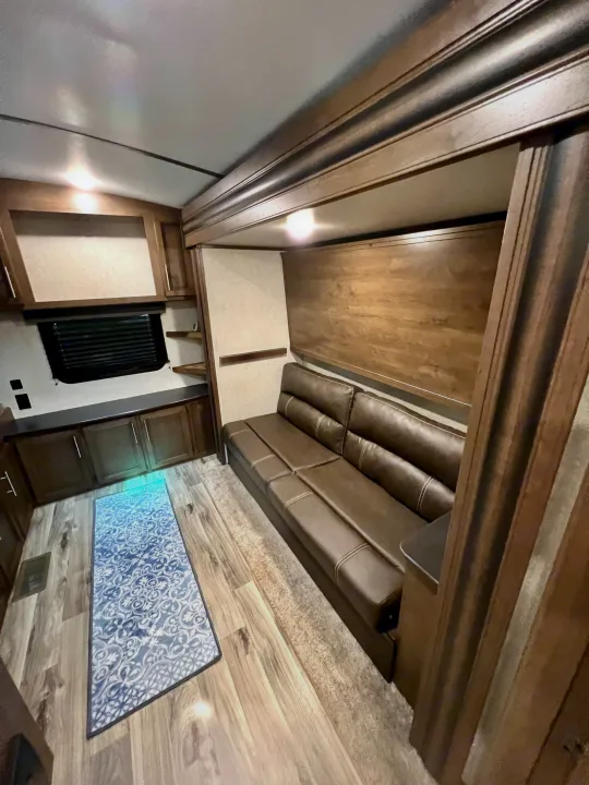 Step inside this modern RV rental! Features a comfortable brown sofa, sleek wood cabinetry, and laminate flooring for a cozy living space.. Keystone Cougar Half-Ton 2021