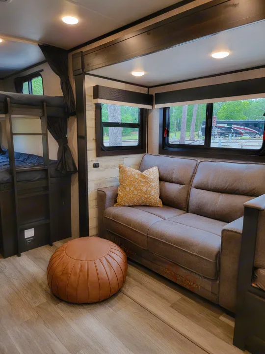 Cozy RV rental interior featuring a gray sofa, bunk beds, and a pouf, with campground views.. Jayco Jay Feather 2023
