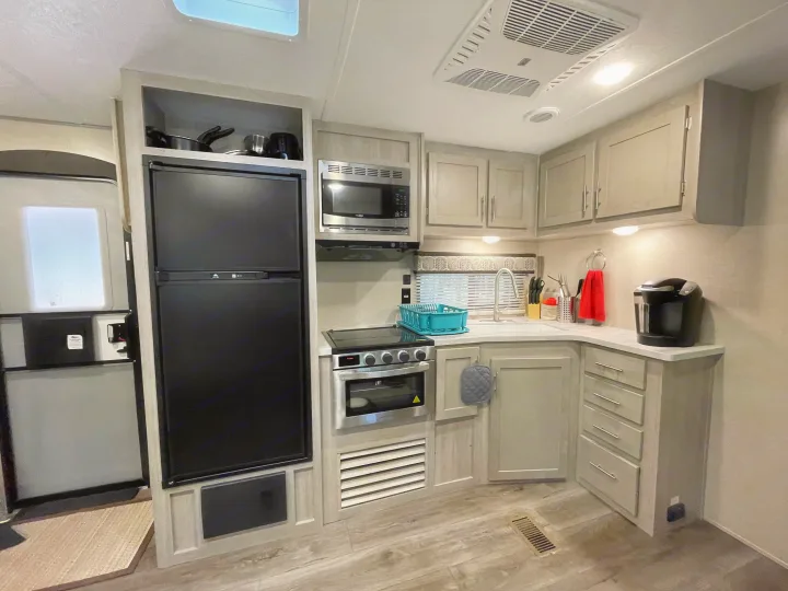 Modern RV rental kitchen with black refrigerator, microwave, stove, and light cabinets, fully equipped for travel.. Forest River Coachmen Catalina Legacy 2022