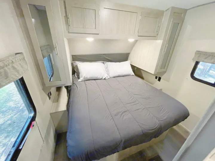 Inside this RV rental, a compact bedroom features a bed with dark bedding, overhead storage, and dual windows for natural light.. Forest River Coachmen Catalina Legacy 2022