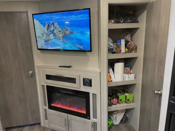 RV rental: a cozy living area with a TV, electric fireplace, and practical pantry shelves for convenience.. Forest River Coachmen Catalina Legacy 2022