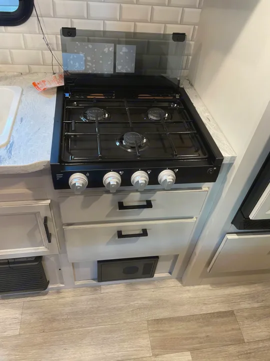 Compact RV rental kitchen with a 3-burner gas stove, sink, and light-colored cabinets. Ideal for road trip cooking!. Jayco Jay Feather 2022