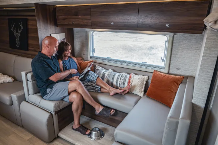 A couple relaxes on a plush sofa inside a modern rv rental, reading a magazine by the large window.. Winnebago View 2025