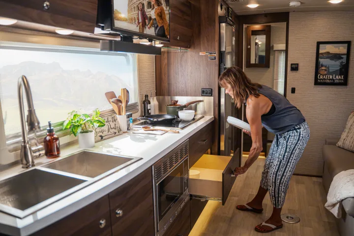 Woman organizing the spacious kitchen in an RV rental, offering comfort on the go with stunning views.. Winnebago View 2025
