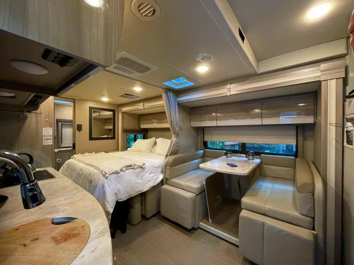 Modern rv rental interior with a comfortable bed, functional dinette, and compact kitchen area for travelers.. Thor Tiburon 2020