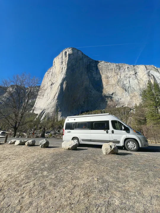 An rv rental camper van rests before Yosemite's El Capitan, a towering granite cliff under a clear sky. A perfect scenic travel spot!. Winnebago Travato 2019