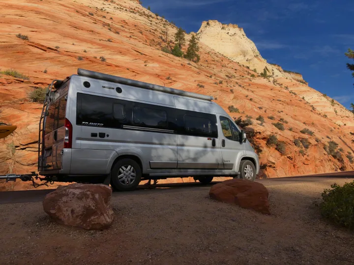 Winnebago Travato RV rental at a scenic pull-off. Silver van, red rock mountains, blue sky, and a kayak.. Winnebago Travato 2019