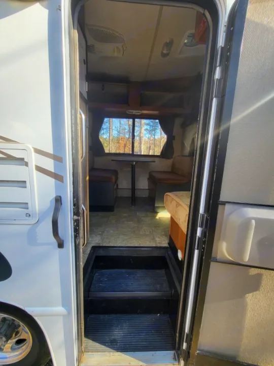 View into an rv rental: an inviting dinette with a window view of trees, seen past the open entry door and steps.. Thor 2012 Thor 19G 2012