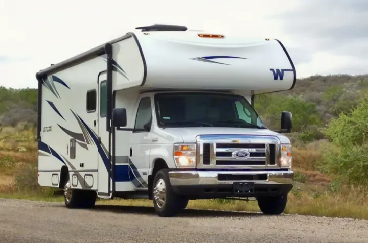 Modern white Winnebago Outlook Class C RV rental parked on a gravel road in a natural setting.. Winnebago Outlook 2019