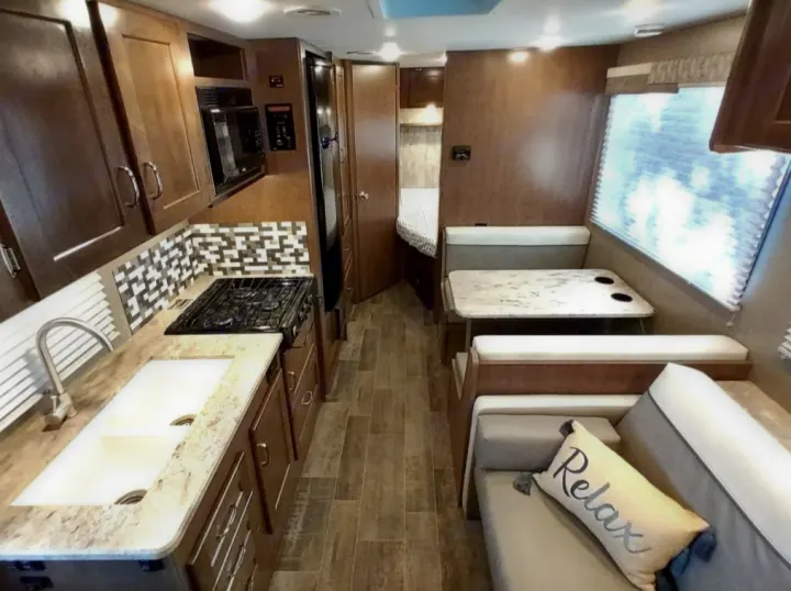 Explore this modern RV rental interior featuring a fully equipped kitchen, dinette, living area, and a glimpse of the bedroom.. Winnebago Outlook 2019