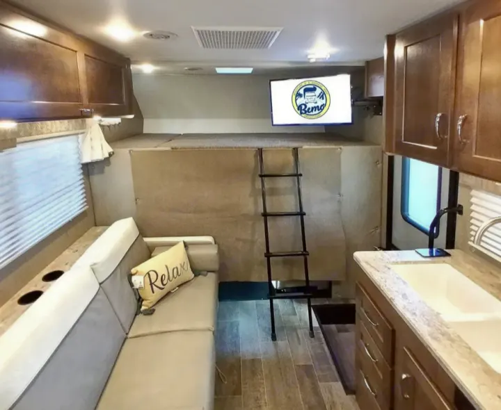 RV rental interior showcasing a living area with sofa, kitchen, TV, and an overhead bunk bed with ladder.. Winnebago Outlook 2019