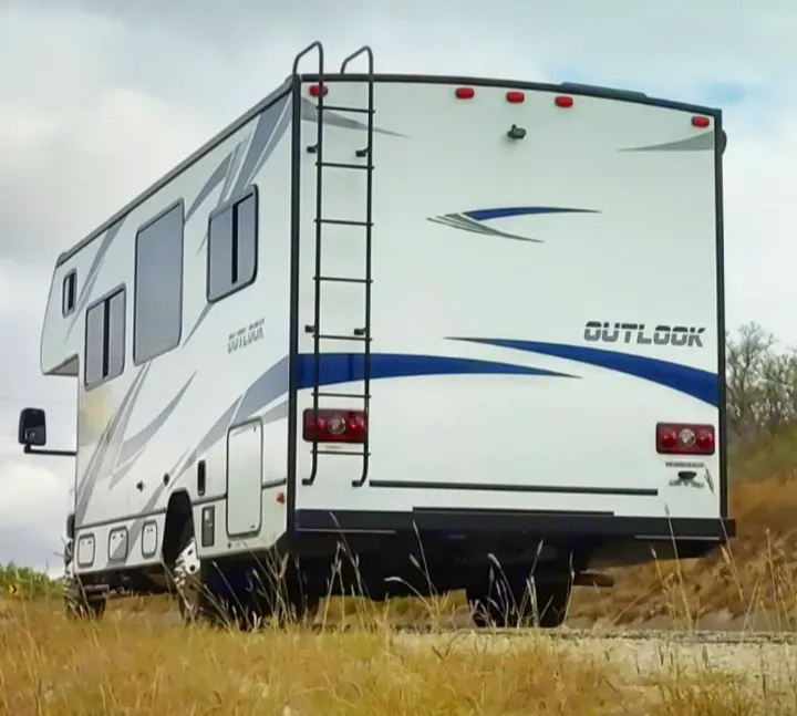 This Winnebago Outlook RV rental on a dirt road, featuring its rear ladder and distinct blue stripes. Ready for your road trip!. Winnebago Outlook 2019