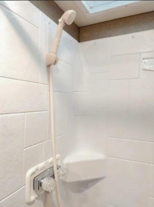 RV rental shower: a compact white stall with a handheld showerhead, built-in corner shelf, and controls.. Winnebago Outlook 2019