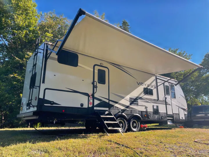 Spacious white and black RV rental travel trailer with extended awning, ideal for your next outdoor adventure or camping trip.. Winnebago Voyage 2021