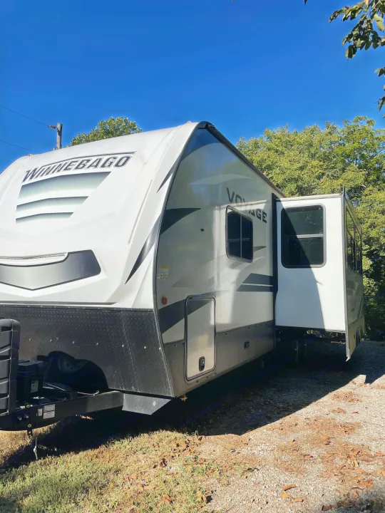 This Winnebago Voyage travel trailer with its slide-out extended is perfect for an RV rental, parked outdoors under a clear blue sky.. Winnebago Voyage 2021