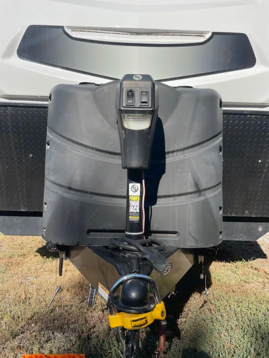RV rental's front: power tongue jack for travel trailer leveling, with propane tank cover & hitch visible.. Winnebago Voyage 2021