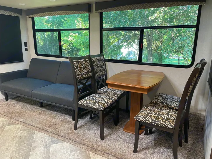 Spacious RV rental interior with comfortable sofa, dining area, and large windows offering a view of nature.. Winnebago Voyage 2021
