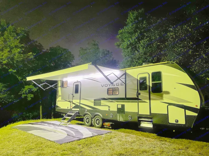 Night view of a bright RV rental with awning lights on, illuminating the steps and mat on the grass. Perfect for camping!. Winnebago Voyage 2021