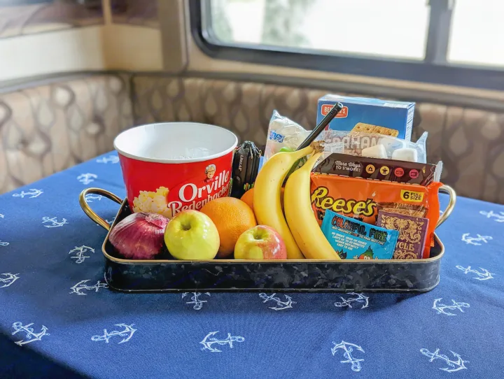 Inside an RV rental, a dark tray holds s'mores ingredients, popcorn, fruit, and fire colorant, all on a blue anchor tablecloth.. Keystone RV Springdale 2013